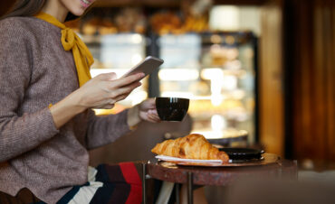 Morning in cafeteria Cute casual girl texting in smartphone while sitting in cafe, having rest and tea with fresh baked pastry