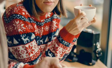 Thoughtful young lady in a Christmas jumper savoring tea at a quaint cafe A contemplative moment as a young woman in a festive jumper enjoys a warm cup of tea, immersed in the coziness of a quaint cafe